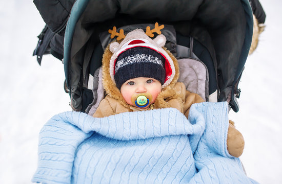 Babywith a pacifier  in a perambulator at a winter day.