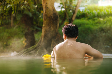 Asian man relaxing in morning is beautiful fog steam hot spring with sunlight  at Hin Dat Hot Spring , Kanchanaburi , Thailand