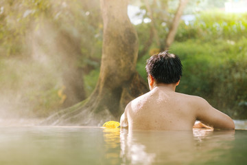Asian man relaxing in morning is beautiful fog steam hot spring with sunlight  at Hin Dat Hot Spring , Kanchanaburi , Thailand
