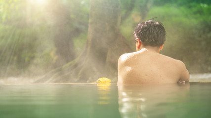 Asian man relaxing in morning is beautiful fog steam hot spring with sunlight  at Hin Dat Hot Spring , Kanchanaburi , Thailand