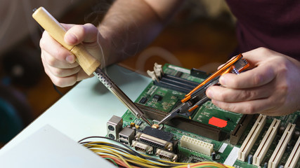 Repair motherboard. Man with a soldering iron and pliers solders the part from the motherboard....