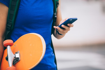 Woman with skateboard in hand using smartphone in modern city