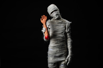 Studio shot portrait  of young man in costume  dressed as a halloween  cosplay of scary mummy holding fake human hand acting on isolated black background.