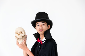 Young Asian boy in black cover and black hat holding and looking to skull. Concept for funny costume in halloween festival