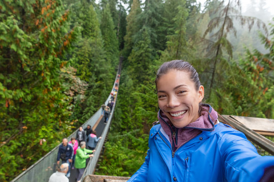 Canada travel tourist woman taking selfie photo at Capilano Suspension Bridge in Vancouver, British Columbia, canadian vacation destination for tourist. Asian girl talking to camera phone.