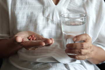 elderly woman are  eating medicine and with pills and glass of water at home