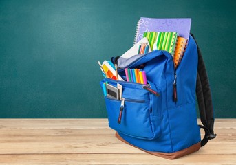 Colorful school supplies in backpack on wooden