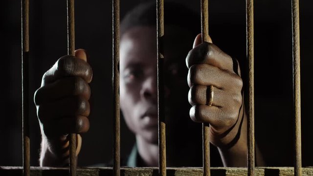 Africa, Migration,illegal. Young black man behind bars in the dark