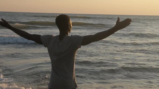 Nature, spirituality, well-being. African man opening his arms on the beach