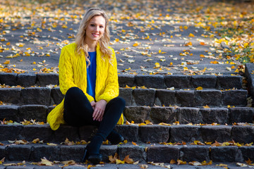 Young, beautiful, blonde woman sits in the park on a old ladder.