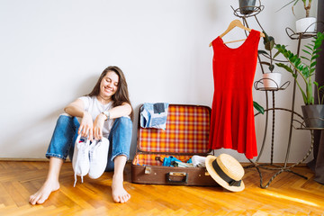 smiling woman sit on floor near valise with clothes. packing before trip. travel concept. copy space