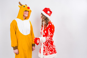 Fun, Christmas and holidays concept - happy woman in santa clothes with man in costume of deer are...