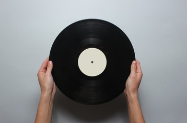 Female hands holding a retro vinyl record on a gray background. Top view, minimalism..