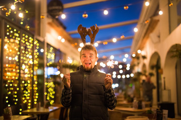 People, holidays and christmas concept - surprised man in deer's horns holding two bengals light or sparklers outdoors