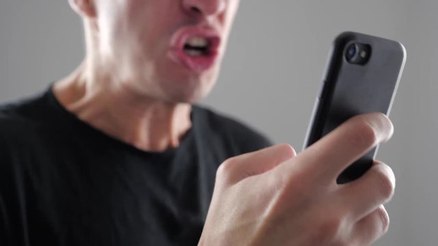 Angry Man Using Smartphone. Furious yelling man with smartphone in hand