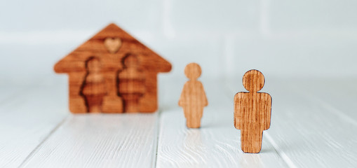Wooden male figure in front of house on grey background