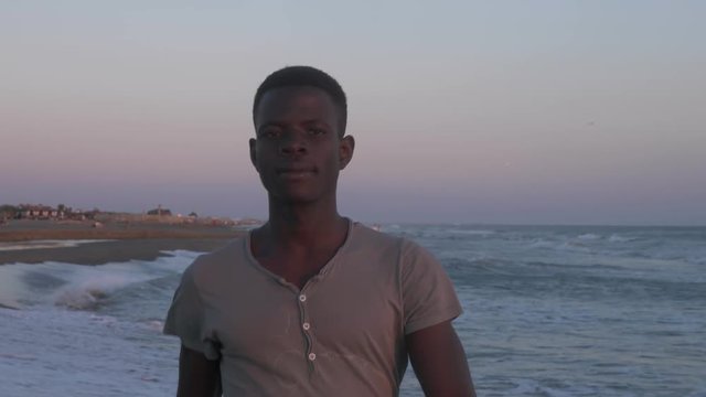 Confident handsome young african man walking on the baech staring at camera