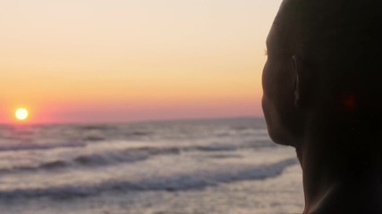 black african man 's silhouette contemplating ocean at sunset - back view