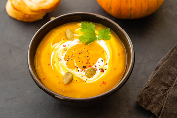 Pumpkin soup in a bowl with fresh pumpkins, garlic and parsley herbs on a black background. Autumn concept.