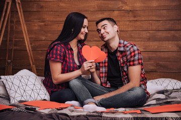 couple in love sits on the bed and red paper hearts on the Valentine's Day. Enamored man and woman...