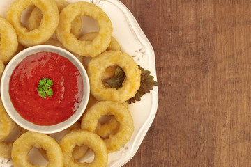 A closeup shot of squid rings with a tomato sauce, shot from above on a dark rustic wooden background with copy space