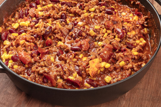 A large cast iron pan with chili con carne on a dark rustic wooden background