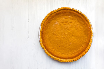 Fresh baked pumpkin pie over white wooden background photographed from above