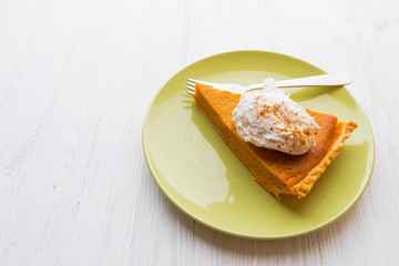 Slice of pumpkin pie with whipped cream over white wooden background