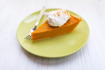 Slice of pumpkin pie with whipped cream over white wooden background