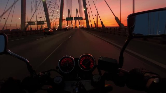 Biker driving a motorcycle rides on the big brige in sunrise. First-person view.