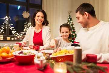 holidays, family and celebration concept - happy mother, father and little daughter having christmas dinner at home