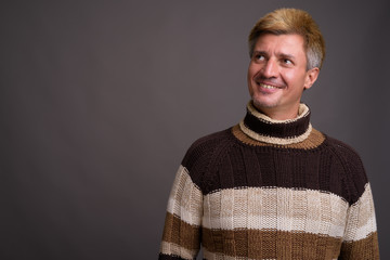 Man with blond hair wearing turtleneck sweater against gray back