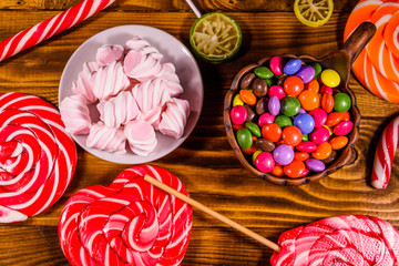 Ceramic plate with marshmallow, candy cane and lollipops on a wooden table. Top view