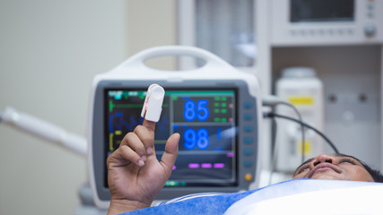 Black male patient lying on operating table connected to vital signs monitor showing heart rate and...
