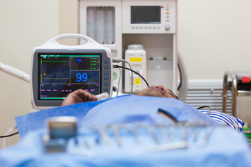 Black male patient lying on operating table connected to vital signs monitor showing heart rate and...
