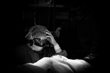 Surgeon wearing protective gear takes a moment of pause during intense surgery under dramatic...