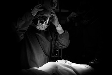 Tired doctor rests with hand on forehead while performing complex surgery, captured in emotional...