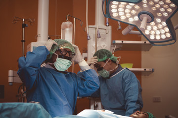 Surgeon wearing protective gear takes a moment of pause during intense surgery under dramatic...