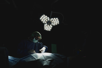 Asian male surgeon focused on critical procedure under surgical light in dark sterile operating...
