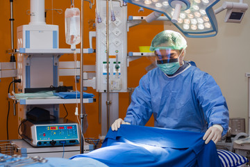 Surgeon in blue sterile gown and mask preparing patient for surgery in modern hospital operating...