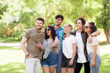 friendship, leisure and technology concept - group of happy smiling friends taking picture by selfie stick at summer park
