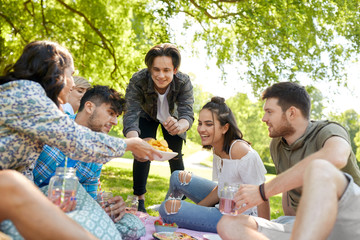 friendship and leisure concept - group of happy friends with non alcoholic drinks and food at picnic in summer park