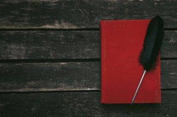 Closed red book and feather pen on the table background with copy space.