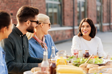 leisure and people concept - happy friends having dinner or bbq party on rooftop in summer