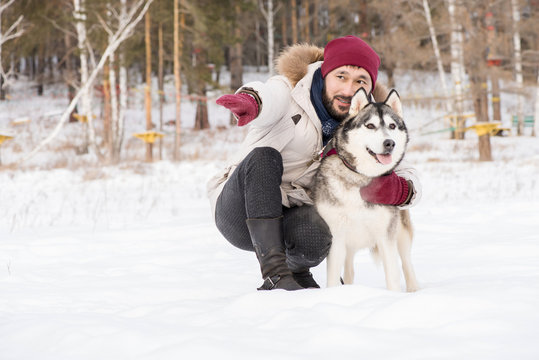 Full length portrait of modern Asian man lovingly talking to gorgeous Husky dog while enjoying time outdoors in winter, copy space