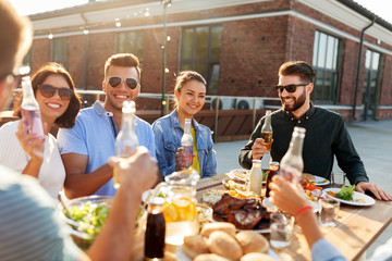 leisure and people concept - happy friends with drinks having barbecue party on rooftop
