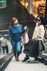 Beautiful girls with paper bags on escalator at supermarket