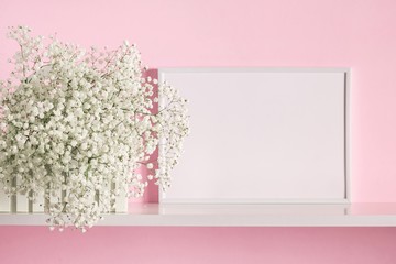 Front view blank mock up of photo frame on the pink background. Small white flowers in vase on pink...