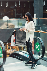 Beautiful girl with paper bags on escalator at supermarket
