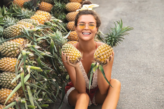 Young and happy woman with a pile of pineapples on the local Thai market